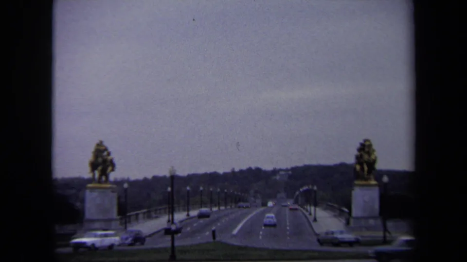 Wide 8mm view of cars on a Washington DC bridge, with equestrian statues at the sides and trees in the distance.