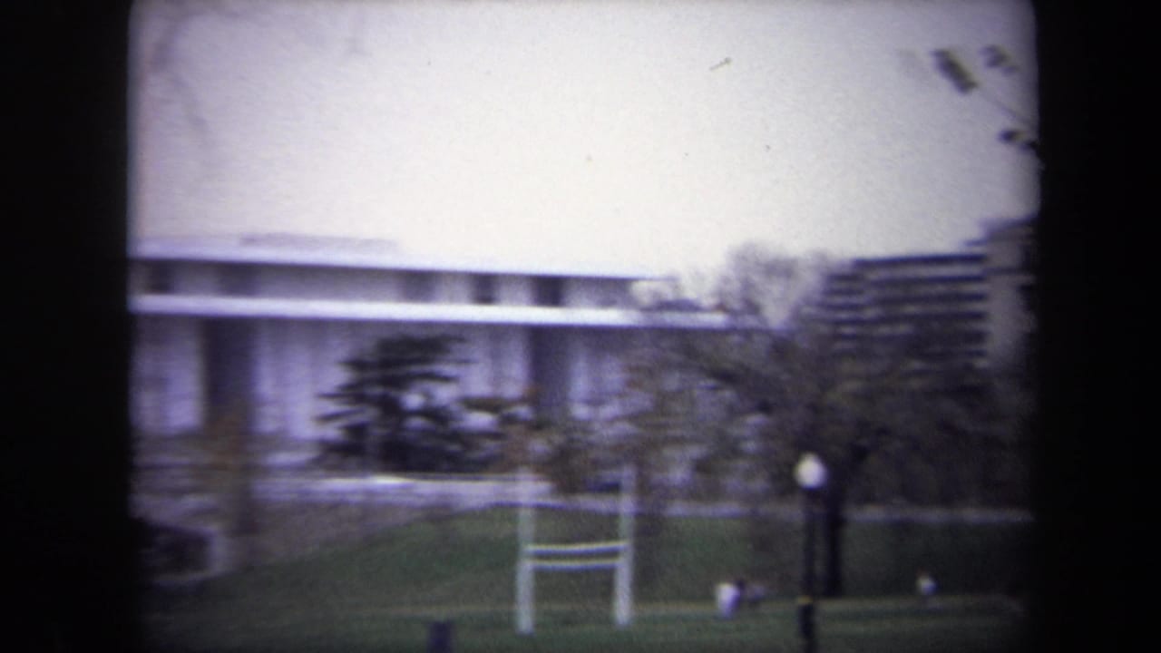 Large white building beyond a grassy lawn with a goalpost and a distant person.