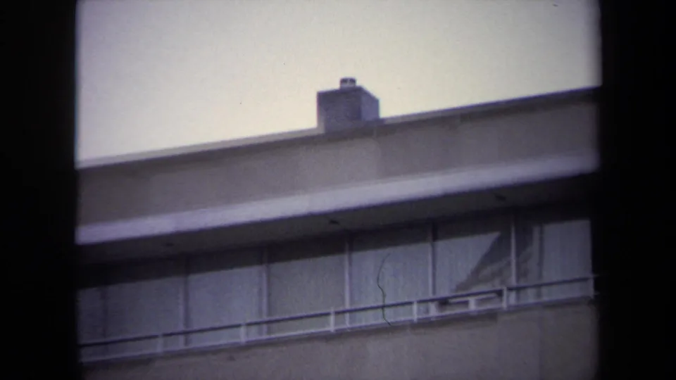 Closer 8mm view of a Washington DC building facade with a flat roofline, chimney, railing, and upper windows.