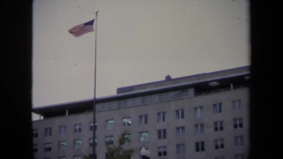 1970 Washington DC frame with a flagpole, American flag, and upper facade of a large government building.