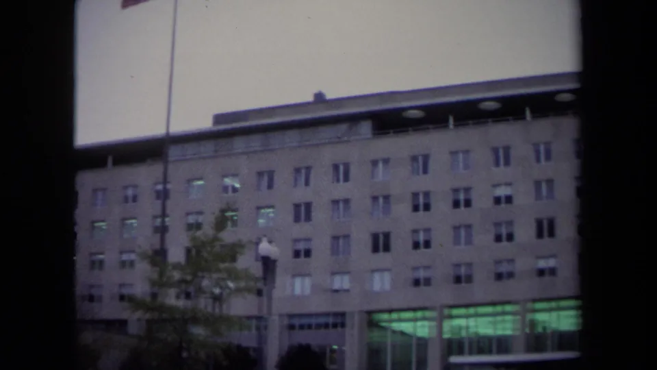 1970 Washington DC frame showing the building's window grid, flagpole, trees, and green-lit ground-floor entrance.