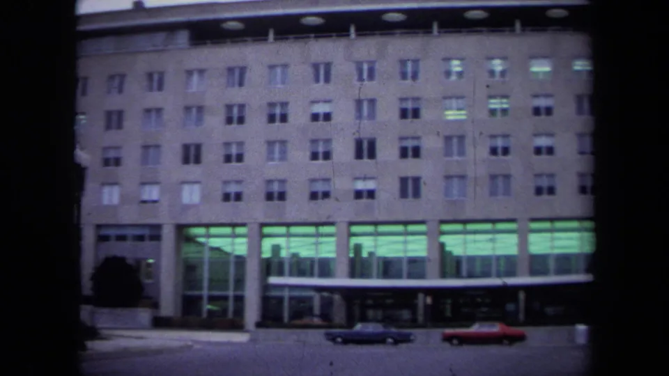 1970 Washington DC frame showing a large government-building entrance with glass bays, columns, and period cars at the curb.