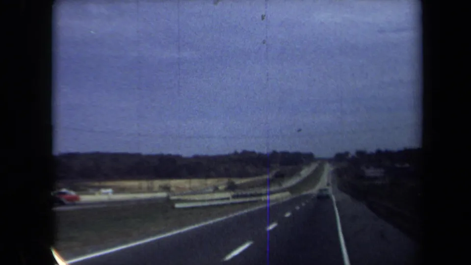 Moving-vehicle view of a broad Washington, DC-area expressway in 1970, with sparse traffic and visible film scratches.
