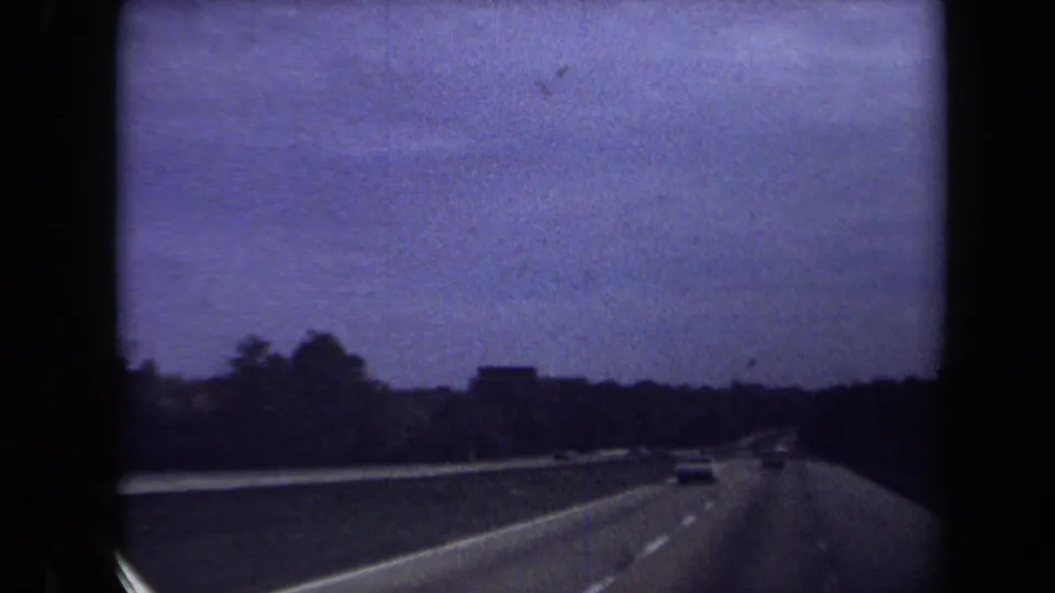 1970 8mm roadway footage shows cars ahead on a divided highway near Washington, DC, with dark trees along the horizon.