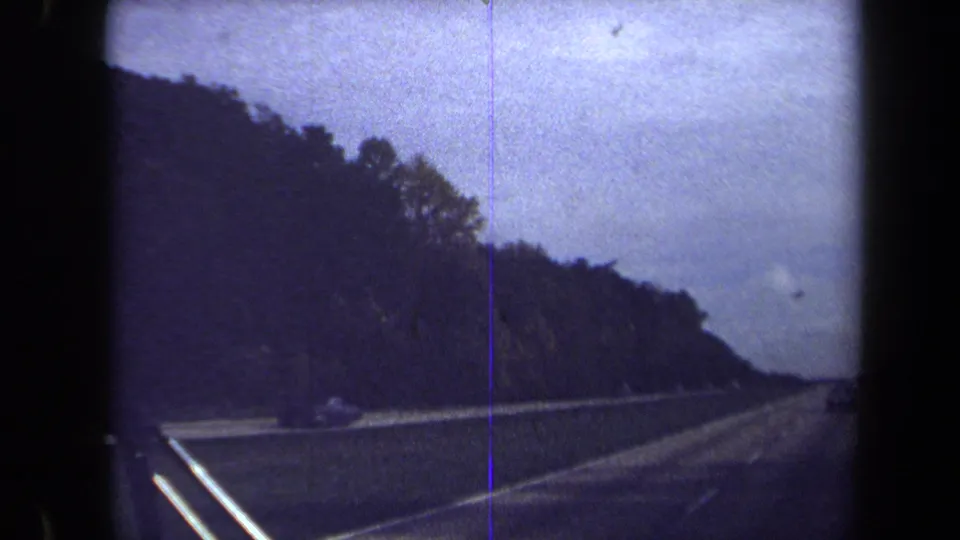 Forward-looking 8mm highway scene in the Washington, DC metadata setting, with wooded roadside, guardrail, and visible film-frame edges.