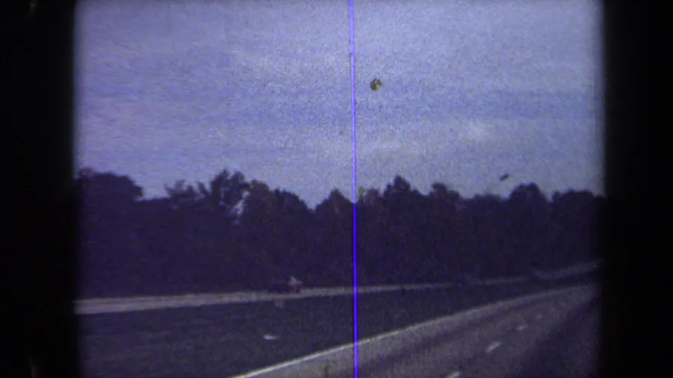 1970 home-movie highway view from the Washington, DC metadata context, showing a road edge, guardrail, trees, and blue-shifted 8mm texture.