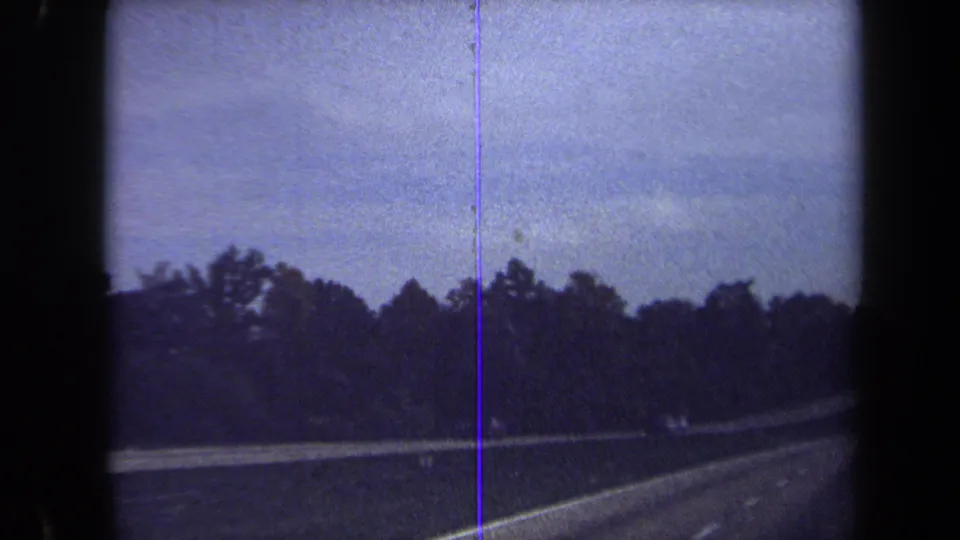 1970 Washington, DC area home-movie frame showing a curving road bordered by trees, guardrail, and a blue-tinted 8mm film edge.