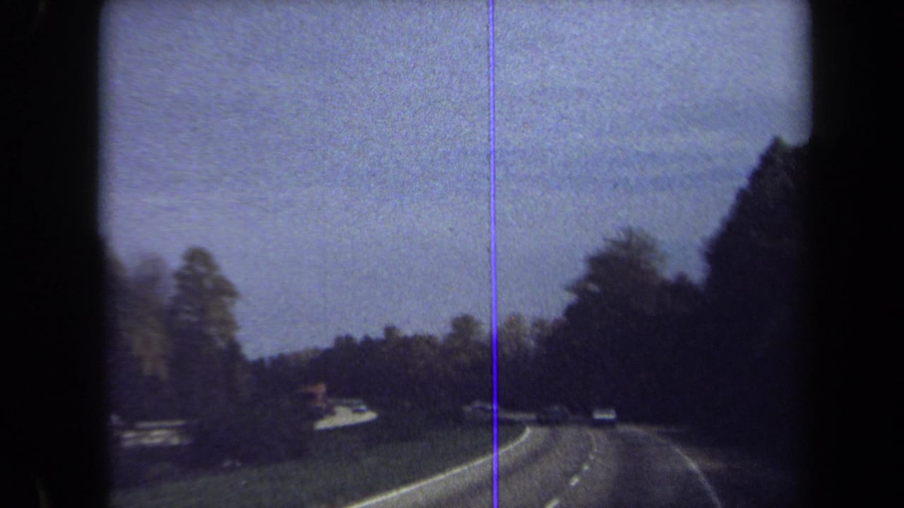Curving multi-lane highway seen through a windshield with trees and cars ahead.