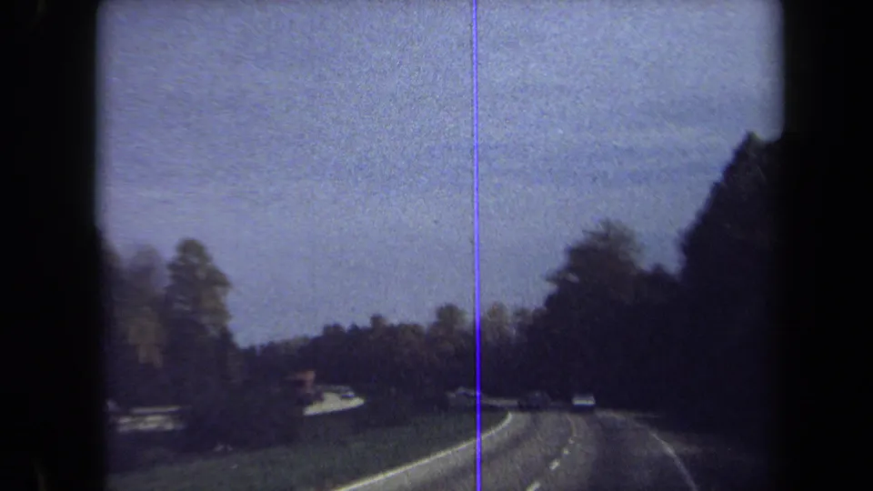 1970 8mm view from a moving vehicle on a wooded Washington, DC-area highway with cars ahead and a pale sky.