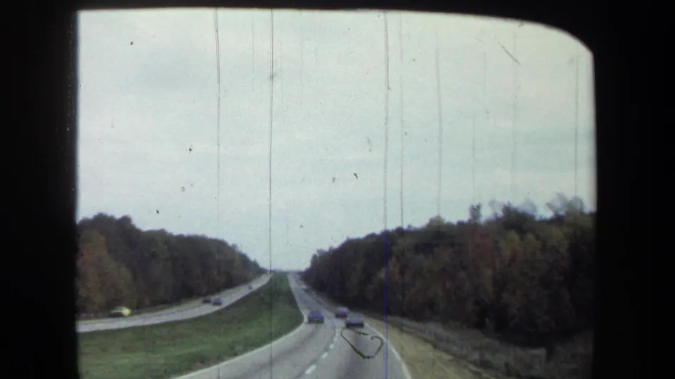 From a moving vehicle, the 8mm frame shows a tree-lined divided highway with cars and a grassy median in 1970 Washington, DC-area footage.