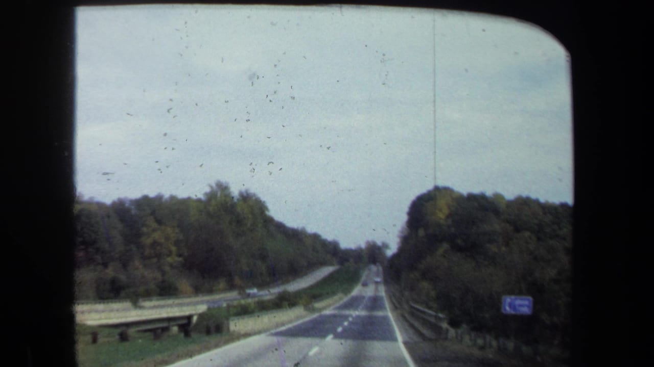 Forward view along a two-lane road bordered by trees and guardrails.