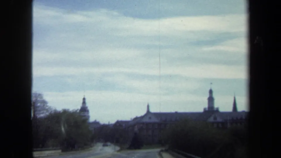Distant view from a moving vehicle of a large towered building in Washington, DC, with trees, roadway, and cloudy sky in the foreground.