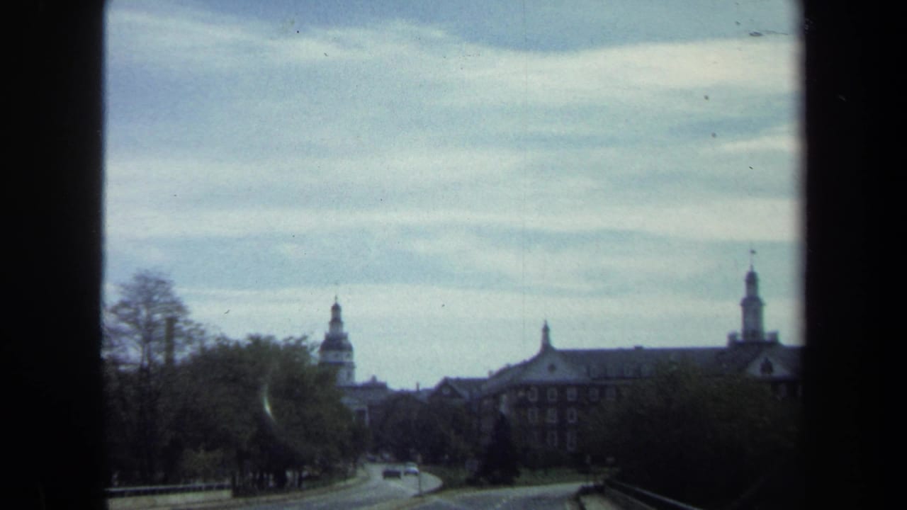 1970 8mm Washington, DC view from a moving vehicle toward domed civic architecture, trees, road, and passing cars.