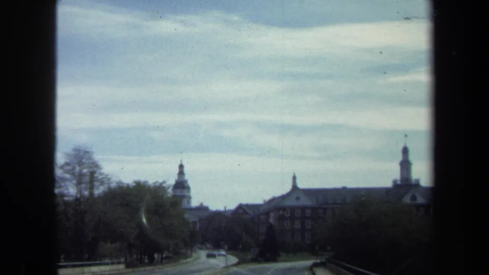 1970 8mm Washington, DC view from a moving vehicle toward domed civic architecture, trees, road, and passing cars.