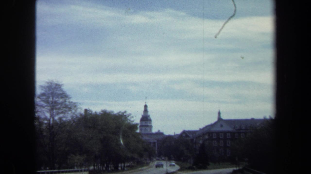 Washington, DC home-movie frame showing cars on a curving road, trees, and a distant domed civic building in 1970-era footage.