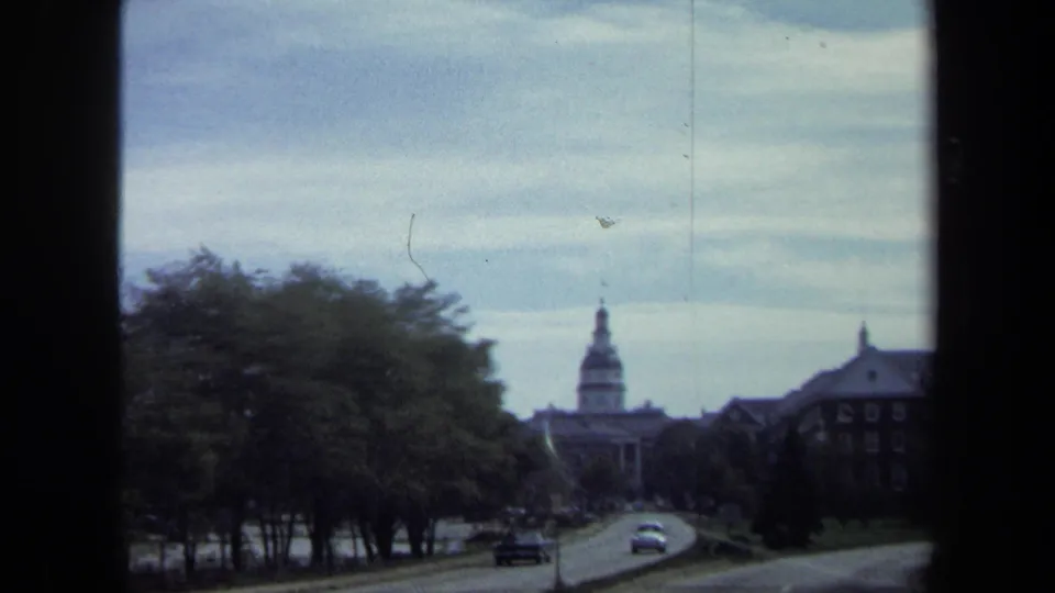 Washington, DC 8mm frame from 1970 showing cars on a road, dense trees, a distant domed building, and adjacent formal architecture.