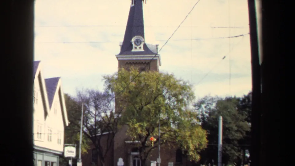 Wider 1970 Washington, DC view of the brick church steeple and clock, seen through a dark window frame with trees and nearby buildings.
