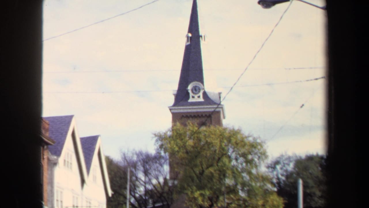 1970 Washington, DC 8mm frame showing a church steeple with cross and clock, partly framed by trees, wires, and a dark window edge.