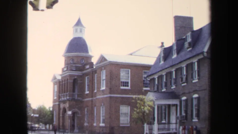 1970 Washington, DC home-movie frame showing a brick building with domed tower, adjacent row houses, sidewalk details, and a distant person.