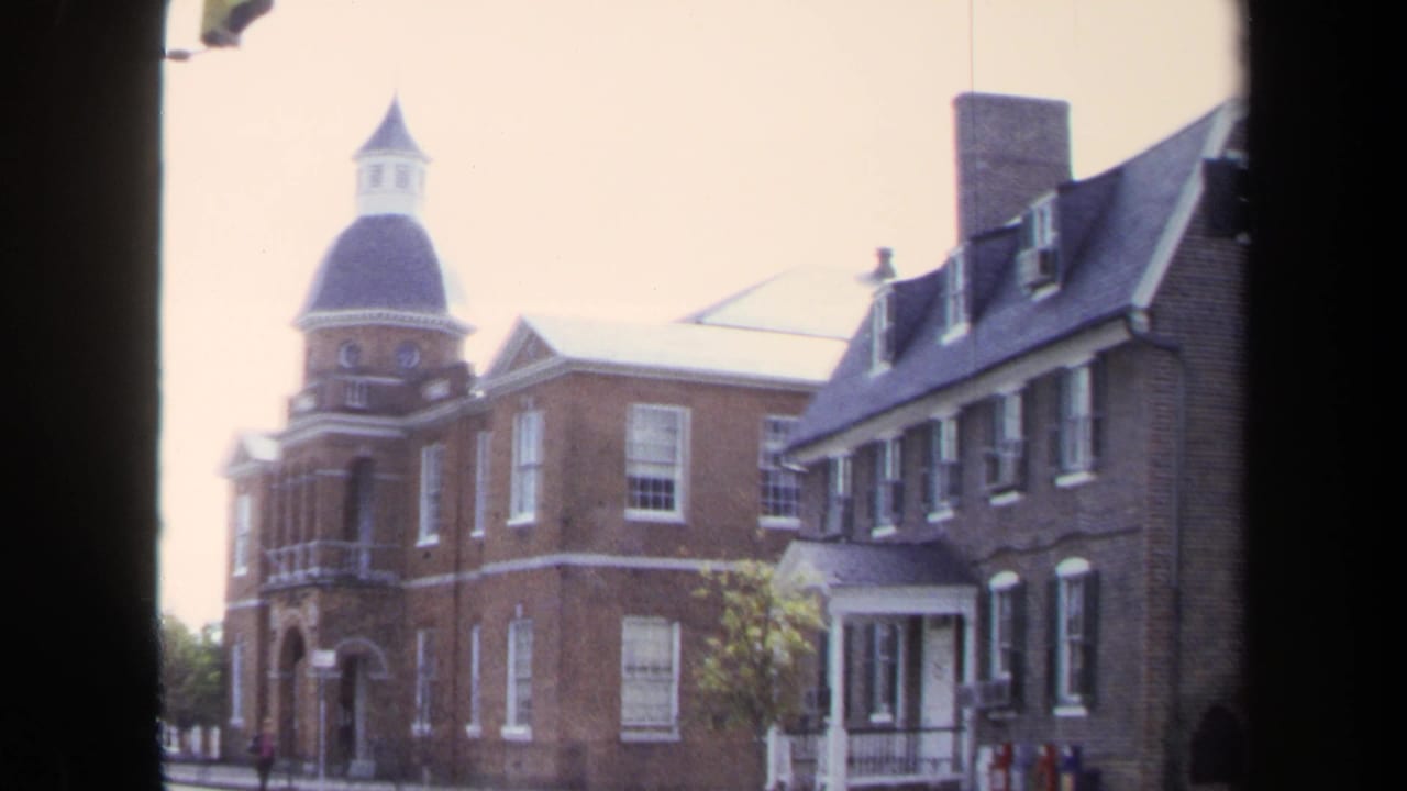 1970 Washington, DC home-movie frame showing a red brick building with a domed cupola and white-trimmed windows through a window frame.