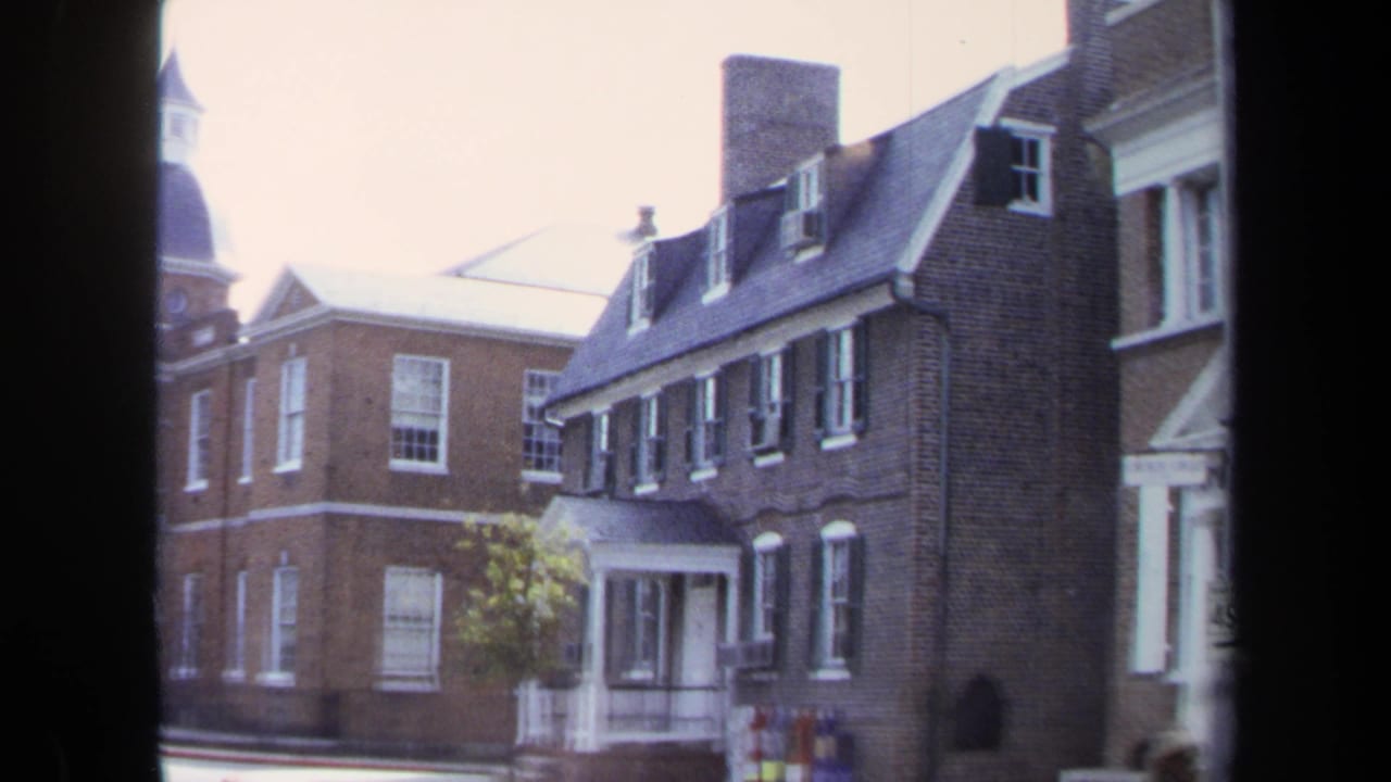 1970 Washington, DC frame with brick buildings, dormers, chimneys, and a cupola partly obscured by a dark vertical window frame.