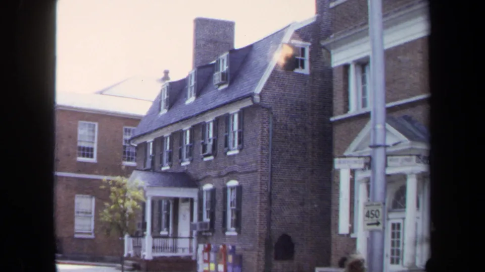 1970 Washington, DC frame showing a brick building with white doorway trim, dormer windows, a 450 street sign, and distant pedestrians.