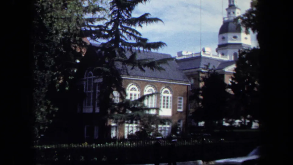 1970 Washington, DC frame showing a brick building with arched windows and cupola, partly obscured by trees and dark window framing.