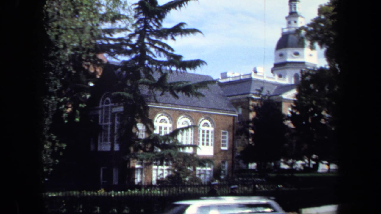 1970 Washington DC 8mm frame showing a red brick institutional building, arched windows, trees, and a domed tower beyond the roofline.
