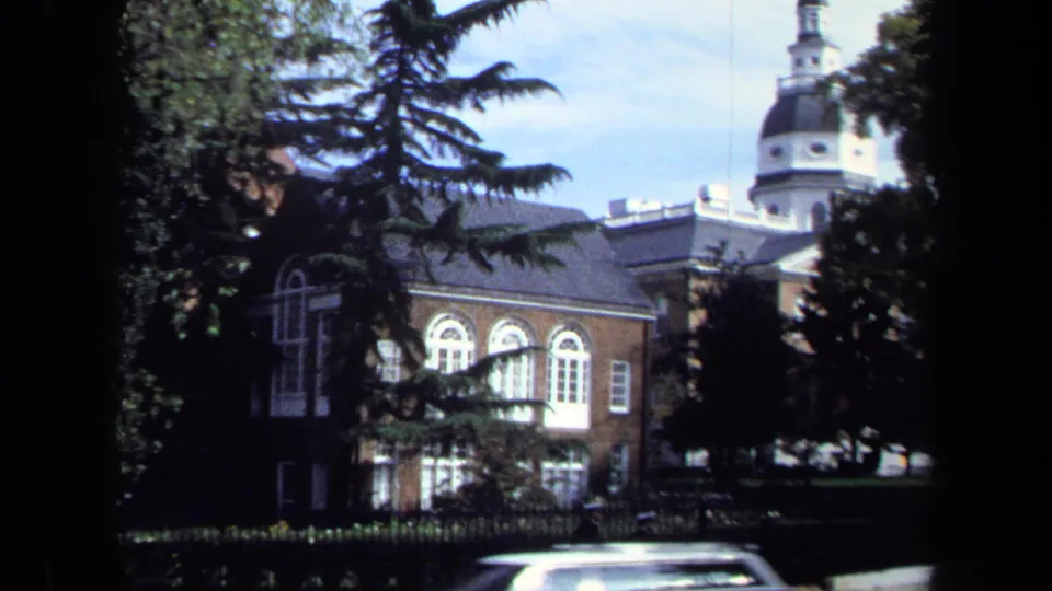 1970 Washington DC 8mm frame showing a red brick institutional building, arched windows, trees, and a domed tower beyond the roofline.