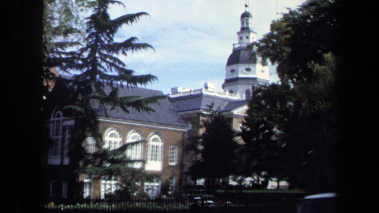 1970 Washington DC home-movie frame with a domed brick building partly obscured by trees and shade from a street-side viewpoint.