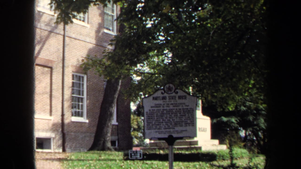 Historical marker for the Maryland State House stands near a brick wall, trees, and lawn in 1970 8mm footage.