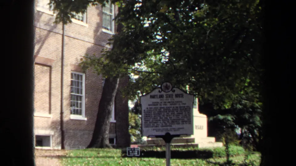 Historical marker for the Maryland State House stands near a brick wall, trees, and lawn in 1970 8mm footage.