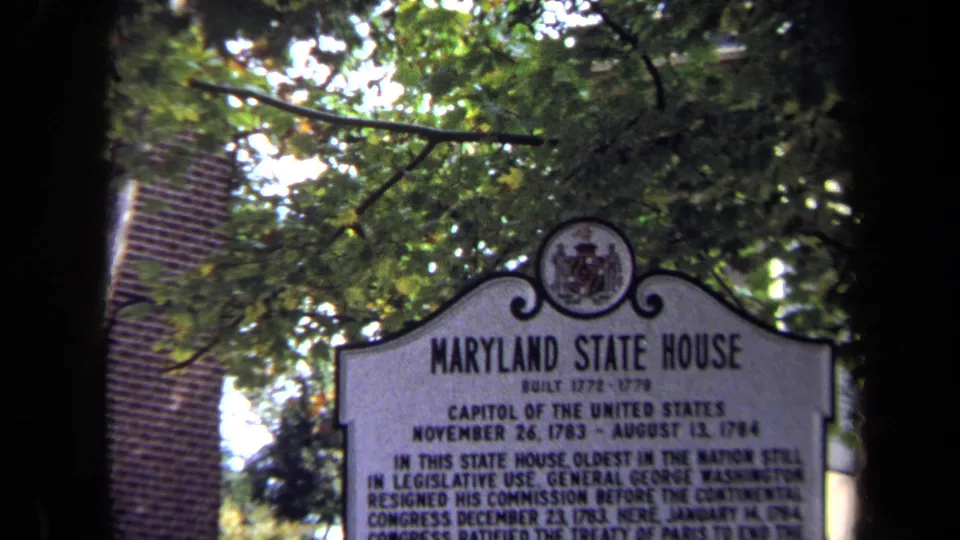 1970 8mm view of the Maryland State House marker, with its title readable above smaller historical text and trees overhead.