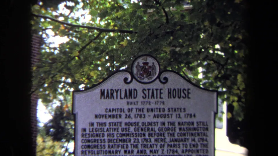 1970 8mm close-up of the Maryland State House marker, showing the title, seal, and dense text beneath a leafy canopy.