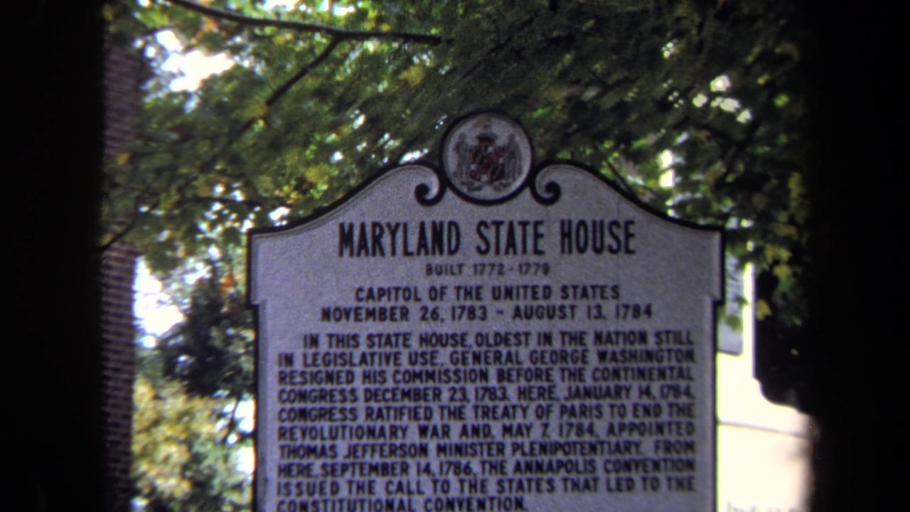 1970 8mm frame of a Maryland State House historical marker with trees, brickwork, and dark frame edges around the sign.
