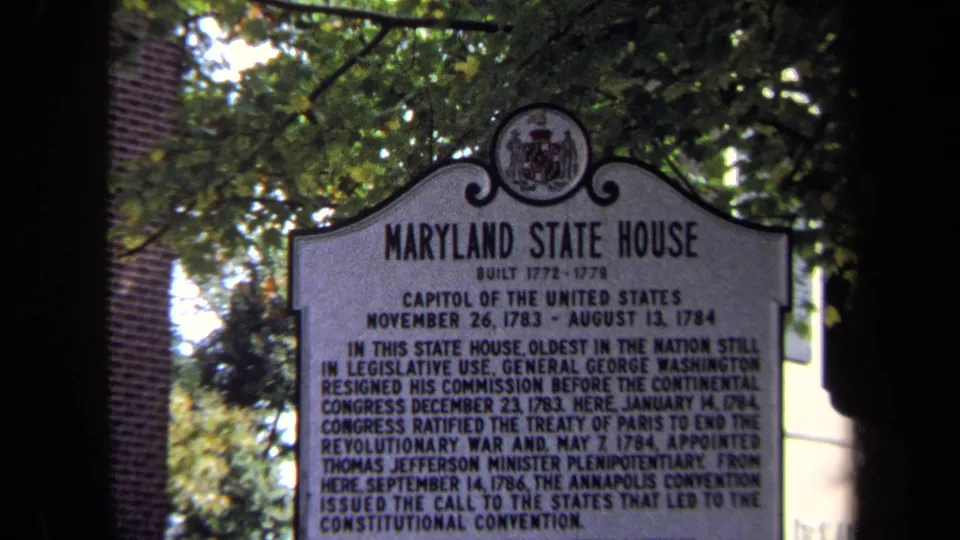 A softly focused 8mm view centers the Maryland State House marker, with dense lettering, crest detail, foliage, and brick behind it.