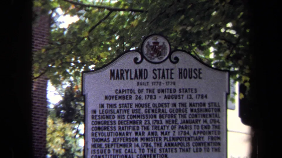 Final frame holds on the Maryland State House marker, with black lettering, overhead leaves, brick background, and strong dark edge shadow.