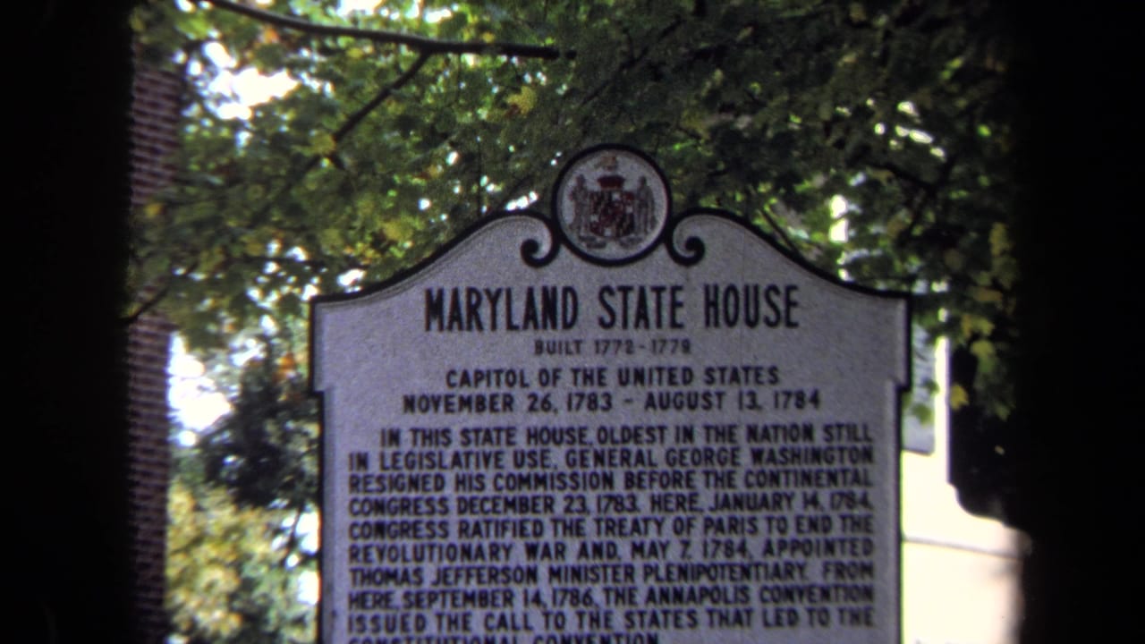 1970 8mm frame of a Maryland State House historical marker seen through foliage and shadowed foreground framing.