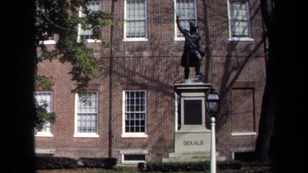 1970 Washington, DC home-movie frame with the DeKalb statue, a lamppost, brick facade, windows, and tree shadows.