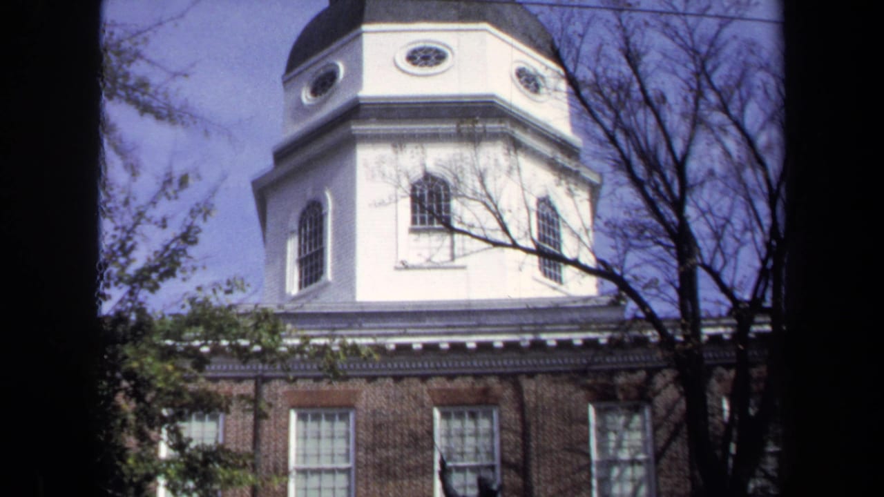 1970 Washington DC 8mm view looking up at a white church tower with arched windows, brick lower wall, branches, and pale blue sky.