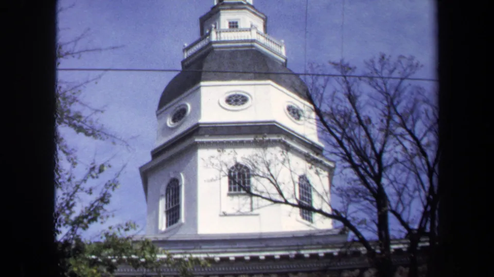 1970 Washington DC exterior frame of a white octagonal church tower with dark roof, lantern cupola, bare branches, utility wire, and blue sky.