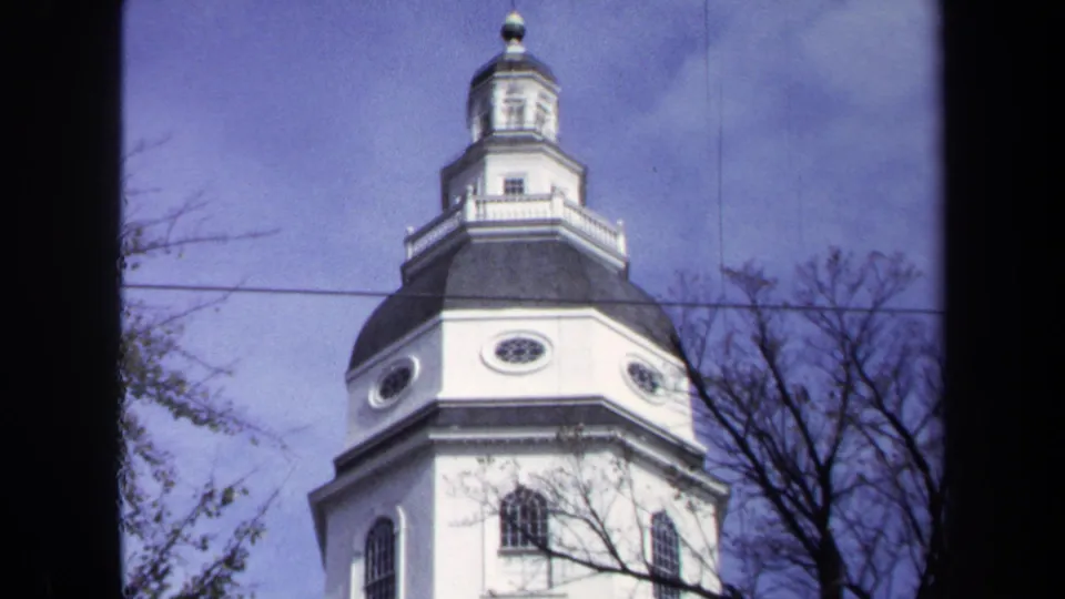 1970 Washington DC 8mm frame showing the church tower's dark roof, white cupola, oval windows, tree branches, utility line, and blue sky.