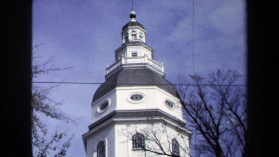1970 Washington DC 8mm view of the white church tower, dark domed roof, lantern top, bare branches, and utility line against a pale blue sky.