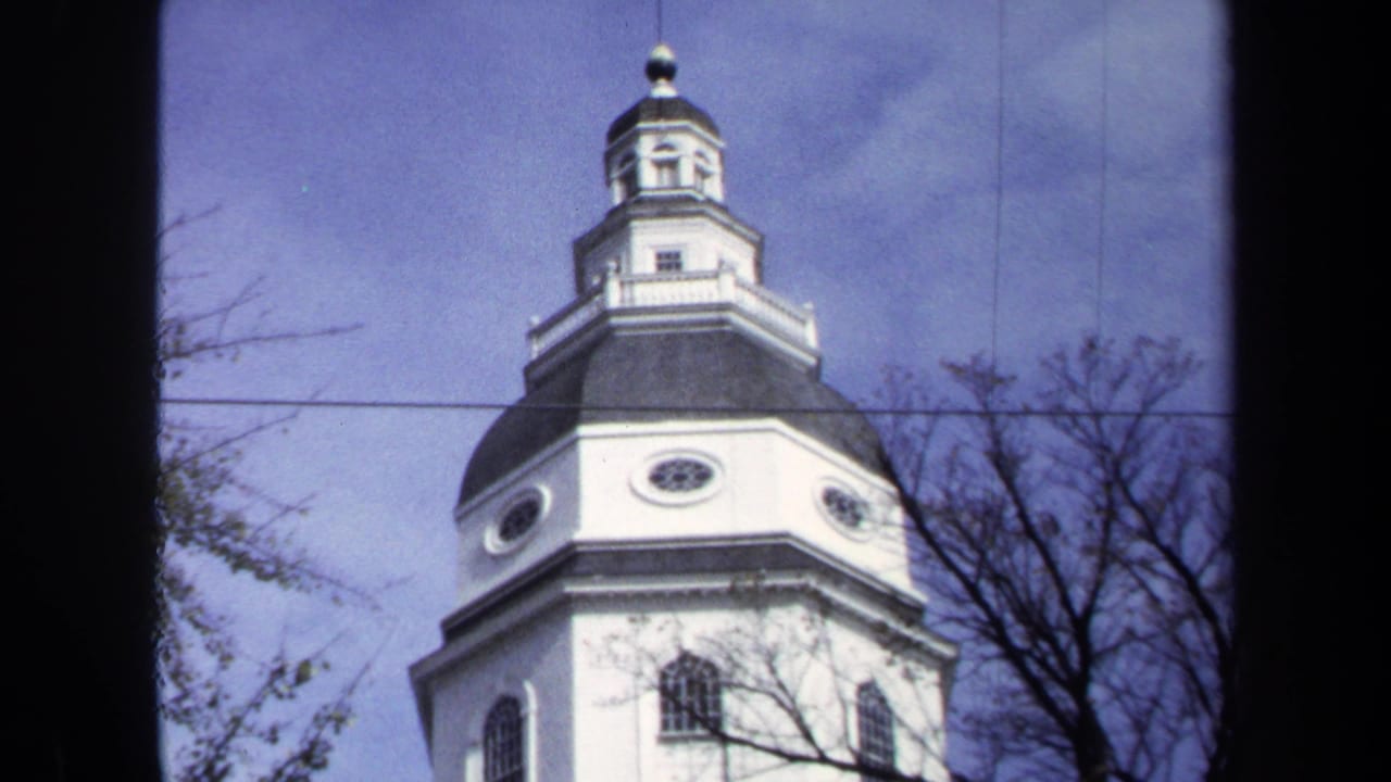 1970 Washington, DC home-movie frame showing a low-angle view of a white historic building cupola framed by bare branches.