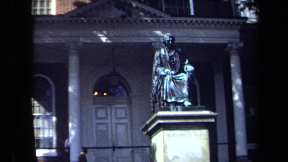 1970 Washington, DC home-movie frame showing a seated monument before a classical building with columns and an arched doorway.