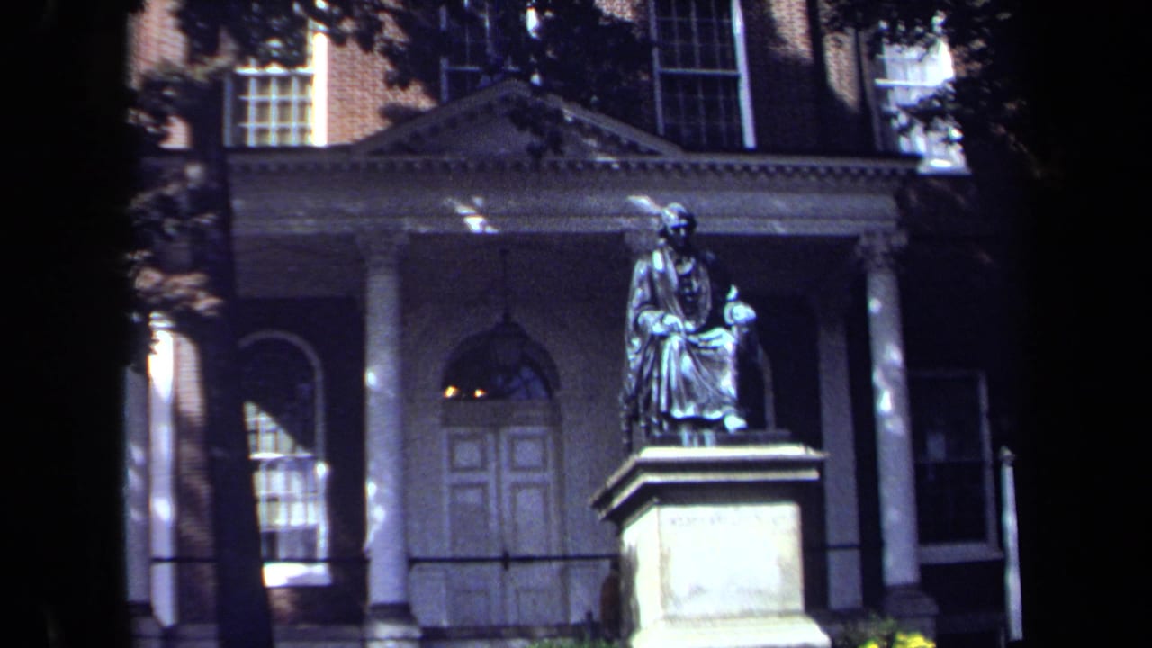 Seated monument centered before a classical entrance with columns and windows.