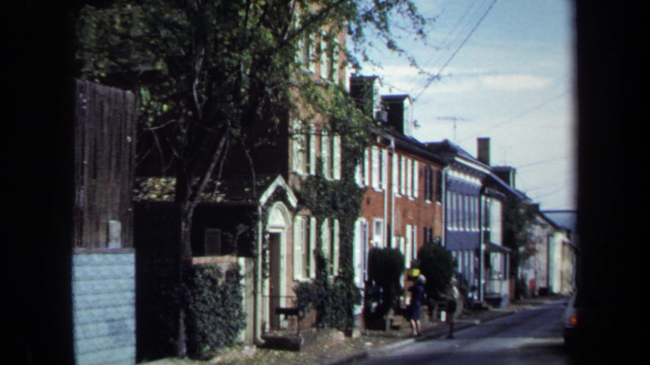 1970 Washington, DC home-movie frame showing two women on a sidewalk beside ivy-covered brick row houses.