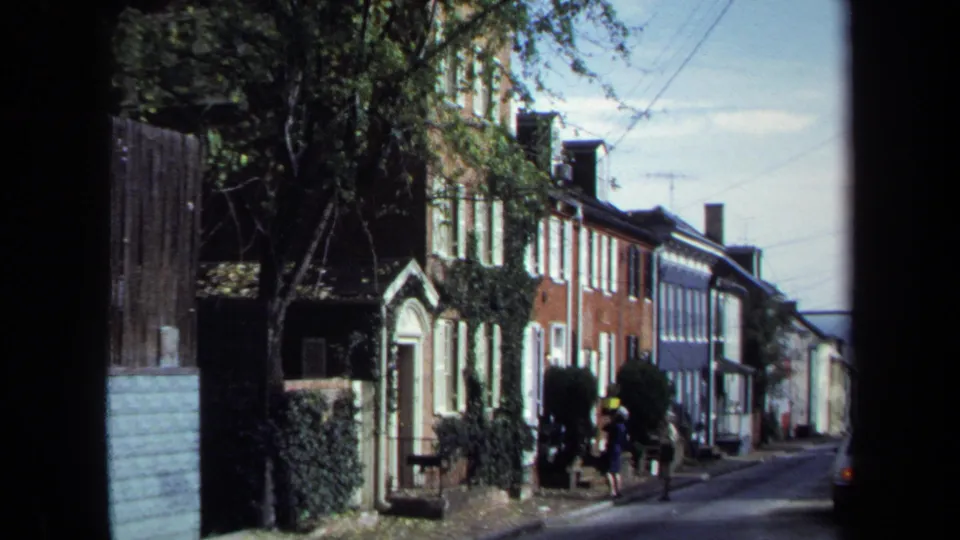 1970 Washington, DC home-movie frame showing two women on a sidewalk beside ivy-covered brick row houses.