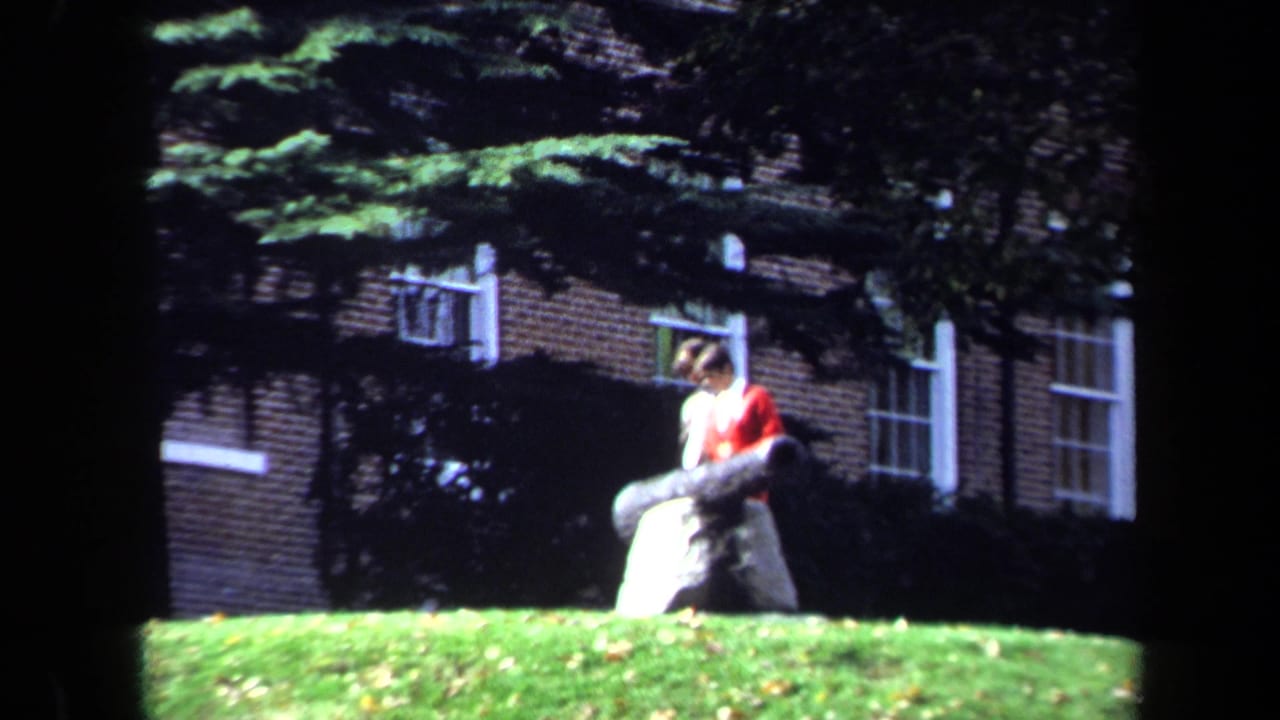 Student in red seated or leaning on a large cannon in front of a brick building.