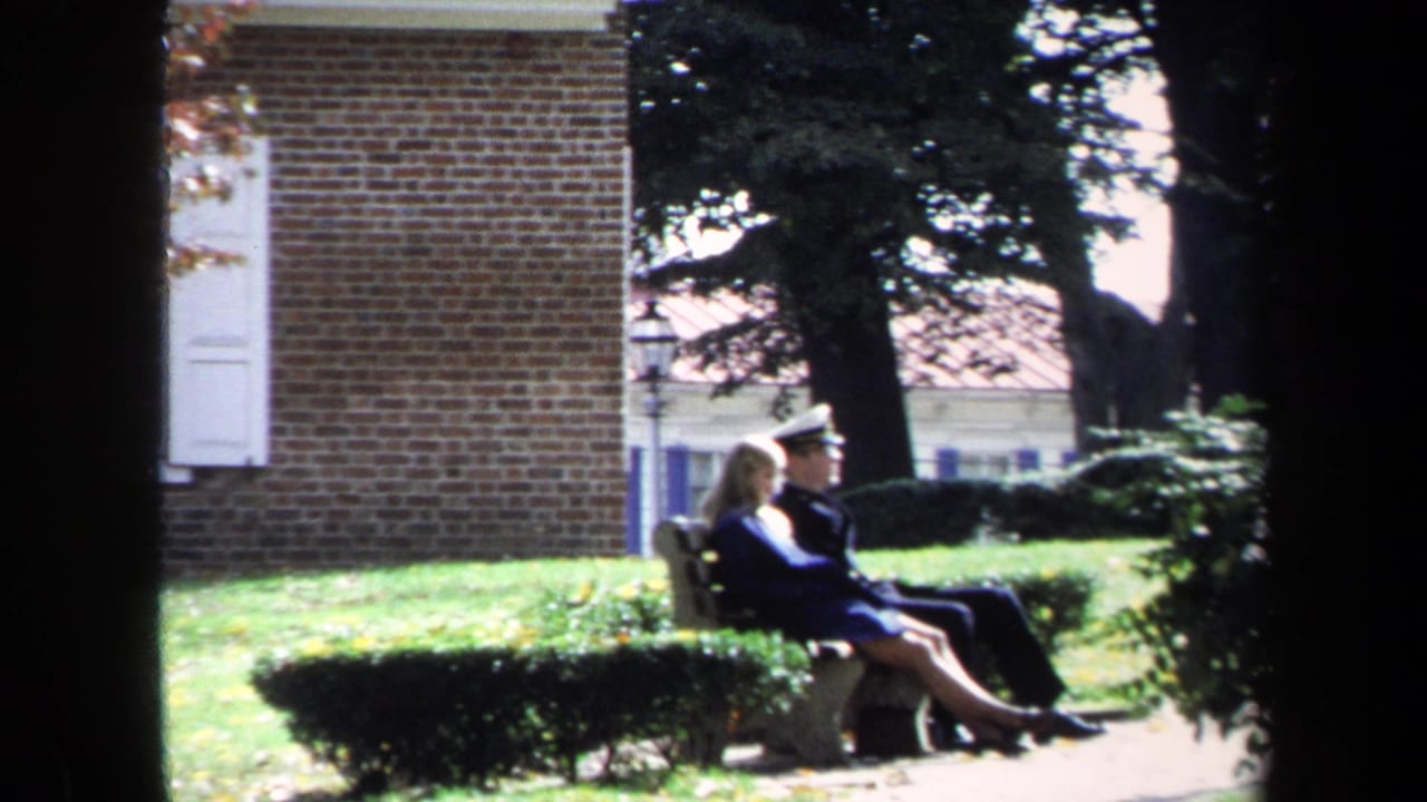 Uniformed man and woman sit on a stone bench beside a brick building.